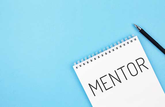 Pen and notebook with word mentor on a blue background