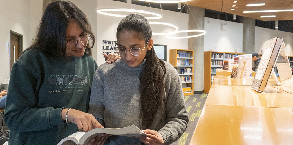 a student helping another student with a book at the library