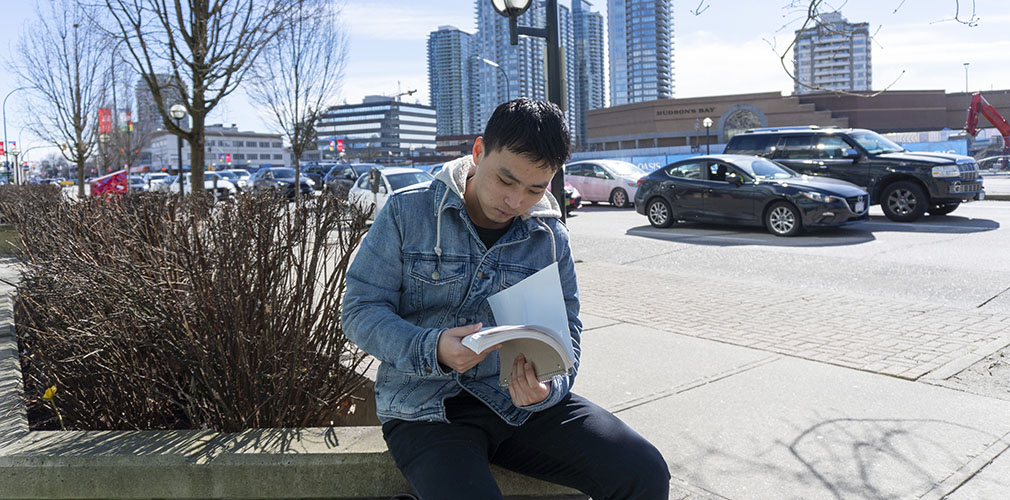 male student reading a book outside