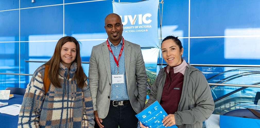 three people standing in front of the UVIC table at teh University Transfer Fair