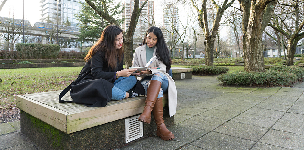 two students looking at a book outside