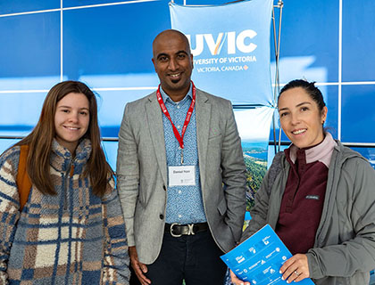 three people standing in front of the UVIC table at the University Transfer Fair