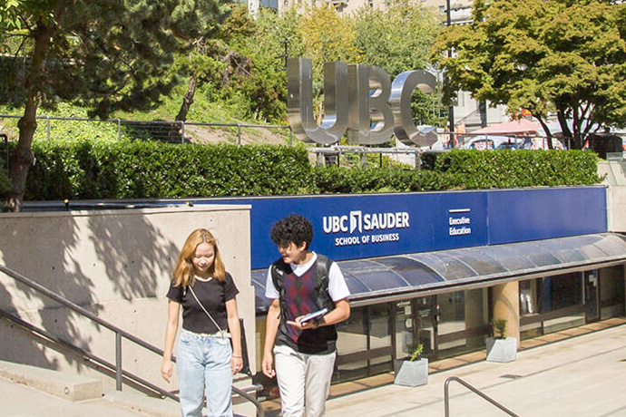 two students walking downtown with the UBC sign in the background